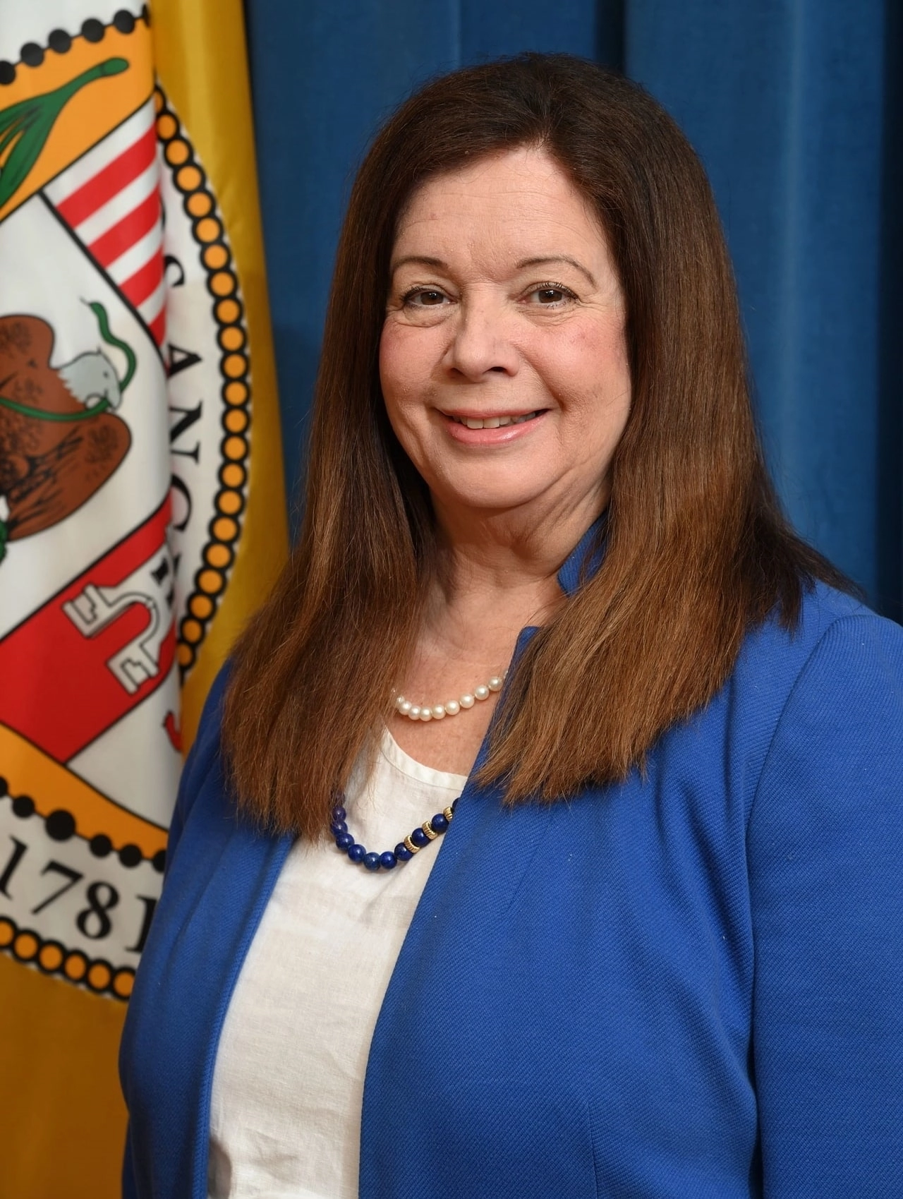 Portait of Los Angeles City Attorney Hydee Feldstein Soto in a blue blazer, standing in front of a blue curtain and flag of the City of Los Angeles.
