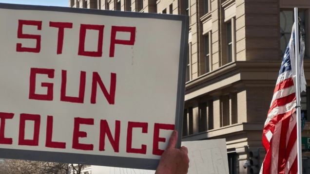 A rally against gun violence and a large sign that says, "Stop Gun Violence." There is also an American flag in the photo