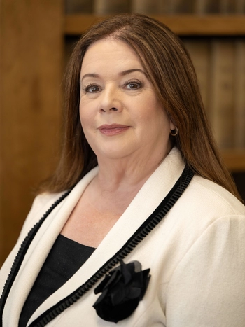 Los Angeles City Attorney Hydee Feldstein Soto in a white jack and black shirt standing in front of a wall of books. She has a black flower pinned to her jacket.