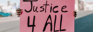 A Black person is holding a large pink sign that has written on it, "Justice 4 all."