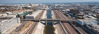 Wide view of a concrete portion of the Los Angeles river, with many buildings and an urban setting surrounding it.
