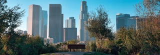 The downtown Los Angeles skyline during the day in the background and in the foreground is the famous bench from the movie, "500 Days of Summer."